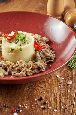 Kırmızı kasede sığır etli patates püresi ve ahşap zemin üzerinde baharatlar olan bir kompozisyon. Restoran yemeği. Kapat.