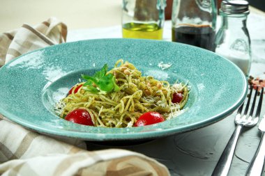 İtalyan spagettisi, pesto soslu ve domatesli. Mutfak malzemeleriyle kompozisyon halinde mavi bir tabakta.