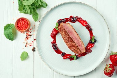 İştah açıcı kızarmış ördek göğsü, beyaz ahşap bir arka planda, içinde malzemeler olan böğürtlen reçeli. Restoran servisi.