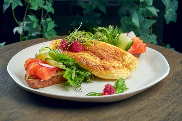 Variation of smorrebrod on rye bread with omelette, cucumbers and salmon in a white plate on a wooden background