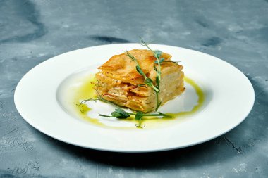 Krem ve peynirli fırında patates graten. Beton arka planda beyaz bir tabakta.