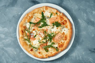 Somonlu peynirli pizza ve gri arka planda beyaz bir tabakta roka. Üst Manzara. Deniz ürünleri pizzası.