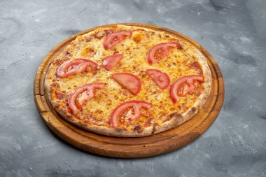 Fırınlanmış İtalyan pizzası, domatesli ve peynirli gri arka planda ahşap tepside.