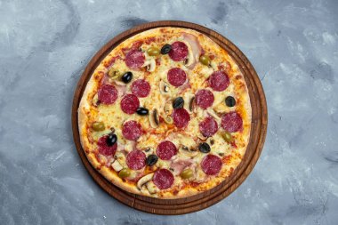 Fırında İtalyan pizzası, salam, zeytin, mantar gri arka planda ahşap tepside..