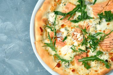 Somonlu peynirli pizza ve gri arka planda beyaz bir tabakta roka. Üst Manzara. Deniz ürünleri pizzası.