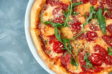 Beyaz tabakta salamlı İtalyan pizzası, roka ve parmesan peyniri. Somut bir geçmiş. Üst görünüm