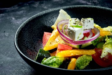 Siyah arka planda domates, soğan, biber ve beyaz peynirli Yunan salatası. Diyet yemek.