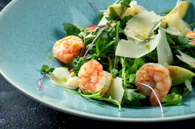 Roka salatası, karides, parmesan peyniri ve siyah arka planda mavi tabakta avokado. Kapatın. Seçici odak