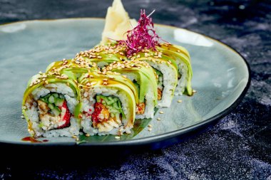 Japon suşisi, siyah arka planda mavi bir tabakta yılan balığı ve avokado ile yuvarlanır. Yuvarlan yeşil ejderha