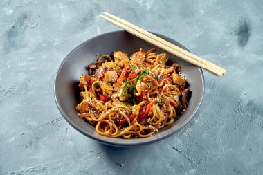 Wok noodle. Gri bir arka planda, tatlı ve ekşi tavuk ve sebzeli udon.