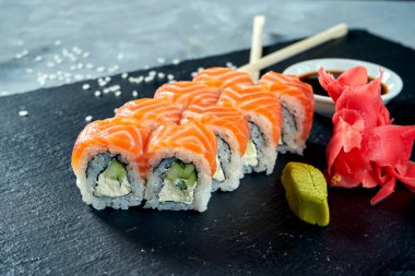 Aperatif Japon suşi ruloları - Philadelphia krem peynirli, salatalıklı ve somonlu gri bir arka planda kara tahtada