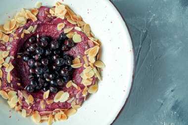 Kahvaltıda yaban mersinli tatlı, reçelli ve bademli gri arka planda beyaz bir kasede.