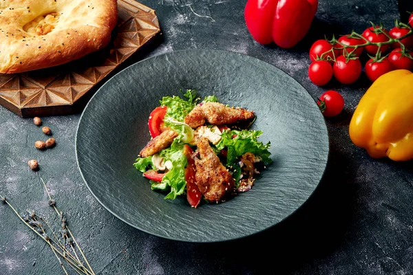 Mantarlı, domatesli, marullu ve siyah tabakta pişmiş tavuklu sağlıklı salata.