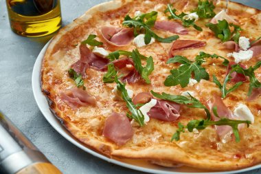 Jamonlu İtalyan pizzası, roka ve gri arka planda krem peynir. Seçici odaklanma, besin düzlüğü