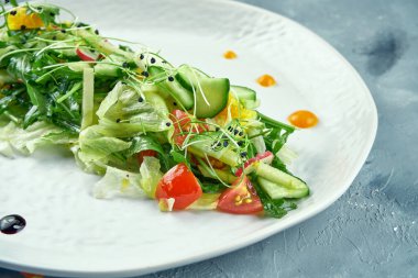 Arugula, domates, portakal ve marul yapraklı Asya usulü vejetaryen salatası gri beton arka planda.