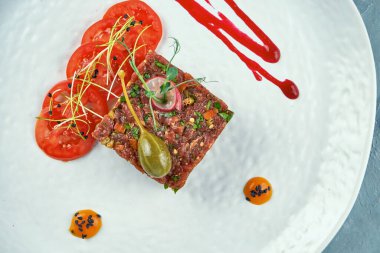 Gri arka planda beyaz bir tabakta kapari, baharat ve soğanlı taze biftekli tartar. Kapatın. Üst görünüm