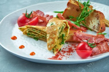 Mükemmel kahvaltı. Ispanaklı omlet, pastırma ve gri arka planda beyaz bir tabakta taze ekmek. Lezzetli omlet.