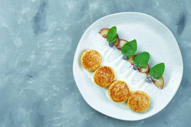 Ekşi kremalı şerbet ve gri arka planda beyaz bir tabakta şeftali. Ukrayna mutfağından peynirli krep.