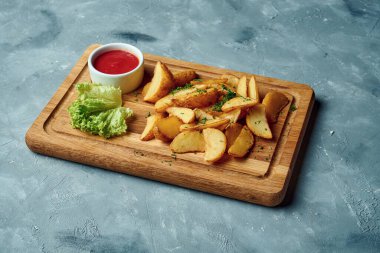 Gri arka planda tahtanın üzerinde pişmiş patatesler iştah açıcı. Patates dilimlerini yakın, fırında kızartılmış.