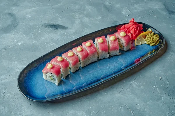 寿司は マグロ クリームチーズ アボカドをグレーの背景に青いプレートで赤い龍を転がします — ストック写真