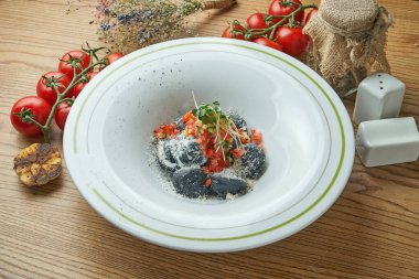 Doldurulmuş siyah hamur köftesi ve ahşap arka planda beyaz bir tabakta domates salçası. Karides ve tavuklu siyah İtalyan mantısı.