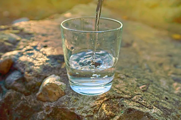 Вода льется в стекло на фоне летней сцены — стоковое фото