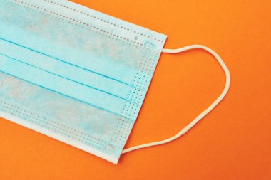 Turuncu arka planda mavi tıbbi maske virüs, koronavirüs, grip, soğuk algınlığı, üst görünüm.