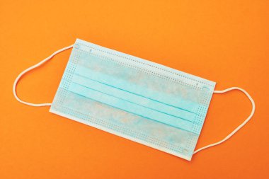 Turuncu arka planda mavi tıbbi maske virüs, koronavirüs, grip, soğuk algınlığı, üst görünüm.