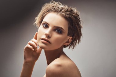 Gri arka planda, çıplak omuzlu çekici bir kadının portresi. Güzel kadın makyaj modeli.