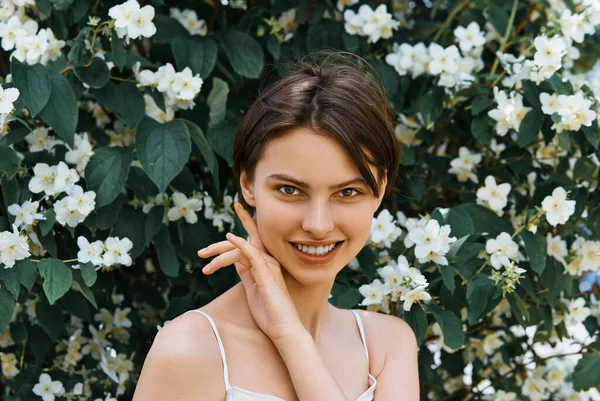 白いドレスで自然の化粧と魅力的な若い女の子屋外 開花ジャスミンブッシュの背景に優しさと柔らかさ — ストック写真