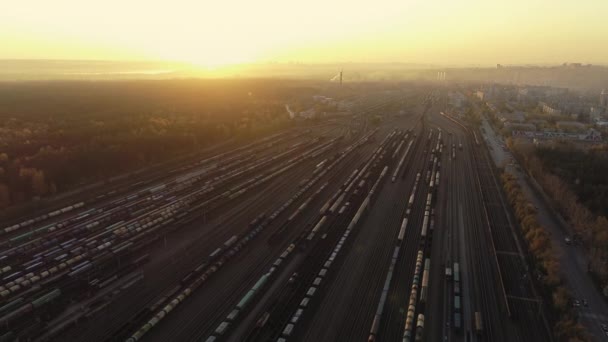 Gün batımında bir drone kamerası demiryolu tasnif istasyonunun üzerine yükseliyor. Birçok vagon ve tren yolu bir endüstriyel yük istasyonunda. Tren raylar boyunca hareket eder. Güzel gün batımı. Ağır sanayi — Stok video