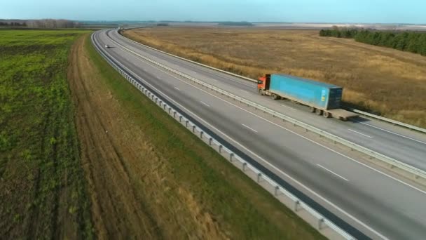 Camioanele și mașinile merg de-a lungul autostrăzii. Privire de sus pe autostradă într-o zi însorită. Maşinile merg pe un drum de asfalt. Autobahn. Vedere aeriană a unei autostrăzi care trece printr-un câmp. transport logistic — Videoclip de stoc