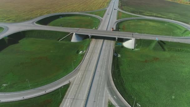 Dron se pohybuje přes dopravní křižovatku. Náklaďáky a auta jedou po dálnici. Cesta za slunečného dne. Autobahn. Nákladní doprava, logistika, nákladní doprava. Krásná pole — Stock video