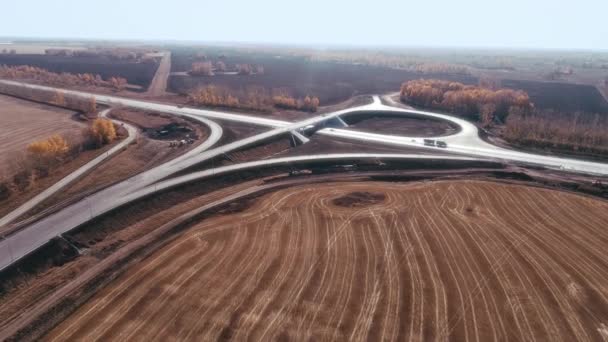 Conexión de transporte. Cruce de carreteras en construcción. Camiones y coches conducen por la carretera. El camino en un día soleado. Logística de transporte. Vista aérea de una intersección de tráfico en los campos — Vídeo de stock