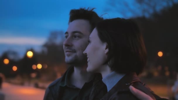 밤 도시의 거리에서 화려 한 빛을 배경으로 한 아름다운 젊은 커플의 근접 사진. 사랑 이야기 로맨틱 한 분위기. 연인두 사람이 포옹하고 일몰을 지켜 봅니다. 여자 — 비디오