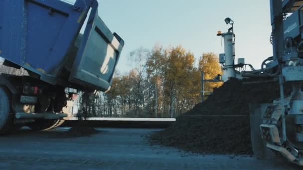 Russia, Novosibirsk Region, July 2, 2020. 노보 시비르 스카도 르. 화물 덤프 트럭은 아스팔트를 섞어 도로 보수 산업을 위해 쏟아 냅니다. 간선도로 건설 공사. 도로 근로자들은 발전 과정을 감시 한다 — 비디오