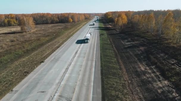 Вантажівки і автомобілі їдуть по шосе. Двостороннє асфальтове шосе в сільській місцевості в літній сонячний день. Верхній вид на автобан. Машини їздять по асфальтній дорозі. Повітряний вид на автостраду. — стокове відео