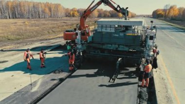 Novosibirsk bölgesi, 2 Temmuz 2020. Novosibirskautor. Otoyol inşaatı. Özel ekipman asfalt kaldırım taşı. İşçiler beton karışımı döşüyorlar. İnsansız hava aracı yolun üzerinden yükseliyor. Yapılan iş...