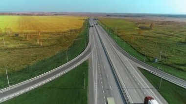 Bir İHA otoban boyunca uçuyor. Kamyonlar otoyol boyunca gidiyor. Güneşli bir günde yol. Otoban 'da. Kargo taşımacılığı, lojistik, kargo teslimatı. Güzel doğa, tarlalar