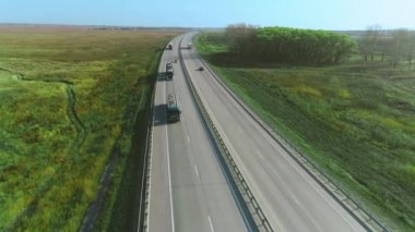 Kamyonlar ve arabalar otoyol boyunca gidiyor. Bir İHA otoban boyunca uçuyor. Güzel doğa, tarlalar. Güneşli bir günde yol. Otoban 'da. Kargo taşımacılığı, lojistik, kargo teslimatı.