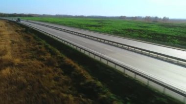 Bir kamyon ve bir araba otoyol boyunca gidiyor. Güneşli bir günde otobanın en üst manzarası. Arabalar asfalt yolda gidiyor. Otoban 'da. Otoyol tarladan geçiyor. Taşıma Lojistiği, Kargo