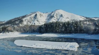 Tatlı su nehri gölünde eriyen buz. Buz ve kardan oluşan donmuş bir tarla. Buz ya da erime. Buzlu karlı dağların arka planının manzarası. Kışın körfez manzaralı dağ manzarası. Kış mavi gökyüzü.