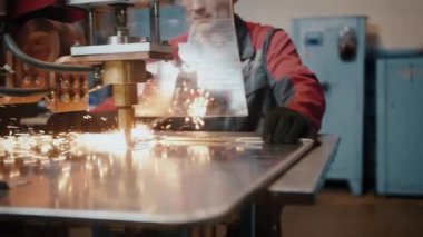 Koruyucu camın arkasında çalışan profesyonel bir işçi lazerle çalışıyor. Sanatçı, mühendis. Lazer kaynaklama. Metal üretiminde yüksek lisans. Çalışırken kıvılcımlar uçuşuyor, kapanıyor.