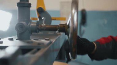 Eldiven ve tulumlu bir işçi makineyi çalıştırıyor. Mühendis el çarkını çevirir. Zanaatkar, metal işçisi. Yakın plan. Yavaş çekim