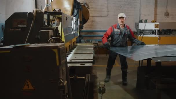 Un ingeniero caucásico profesional está colocando una hoja de metal en una máquina de corte. Maestro, artesano en producción. Máquinas metalúrgicas. Trabajo manual y automatizado en fábrica. — Vídeos de Stock