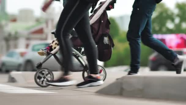 Egy fiatal apa babakocsival átmegy az úton. Átkelés. Városi élet. Névtelen emberek a mashikh hátterében. Lassú mozgás. — Stock videók
