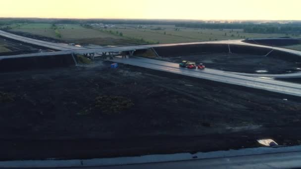 Flight over a road junction under construction at sunset. Road vehicles are standing on fresh asphalt. Beautiful view. New highway. — Stock Video