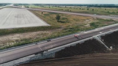 Tulumlu bir grup insan inşaat halindeki yeni bir kavşak boyunca yürüyor. Kuş bakışı. İnsanlar işin ilerleyişini tartışıyor ve takip ediyor. Otoyol kavşağı. Altındaki Yol