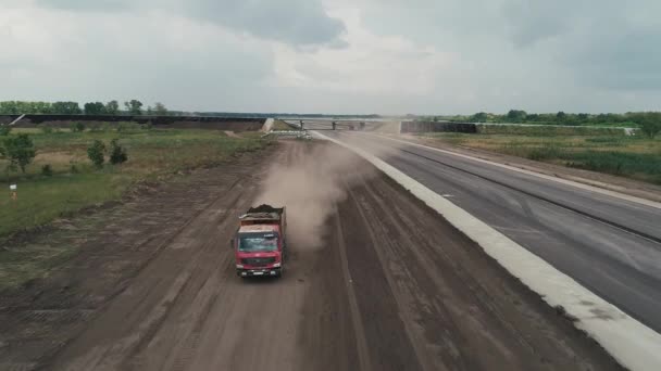 Facendo volare un elicottero davanti a un camion che guida vicino alla strada. Costruzione di un raccordo stradale. Colonna di polvere di un camion di passaggio. — Video Stock