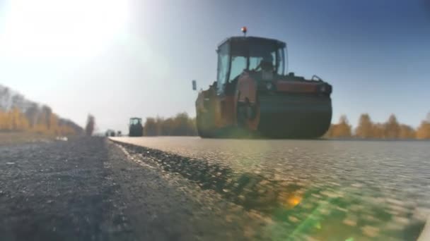 Tir une couche d'asphalte fraîchement posé. Réparation de la chaussée. Construction d'une nouvelle route. Les rouleaux nivelent et compactent l'asphalte. Rouleaux de route. Éblouissement du soleil. — Video